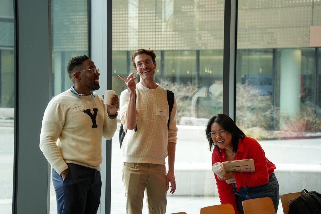 Three colleagues laughing over coffee in a bright, glass-walled atrium
